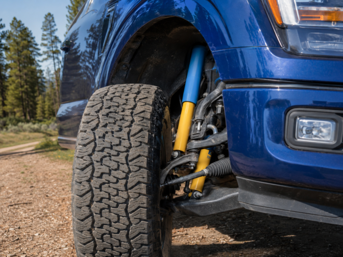 Off-road shock absorber visible behind the front all-terrain tire of a blue Ford F-150