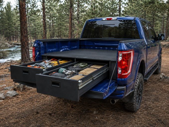 Two long gear drawers open in the bed of Marcus’s blue Ford F-150 at a forest campsite