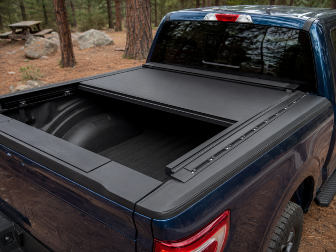 Matte-black retractable tonneau cover partially open over the bed of a blue Ford F-150